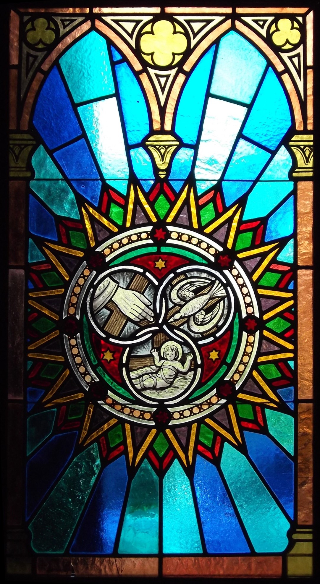 Stained glass window featuring three interlocked circles, with 
			  a hand in the first, a dove in the second, and a baby in the third.